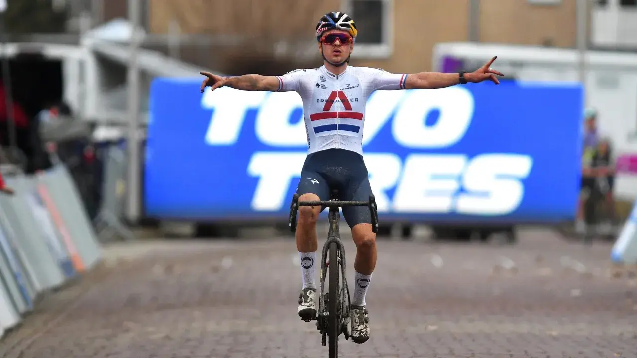 Thomas Pidcock feiert seinen Sieg mit ausgebreiteten Armen. Der Radfahrer trägt ein weißes Trikot mit britischer Flagge und dunkle Hosen.