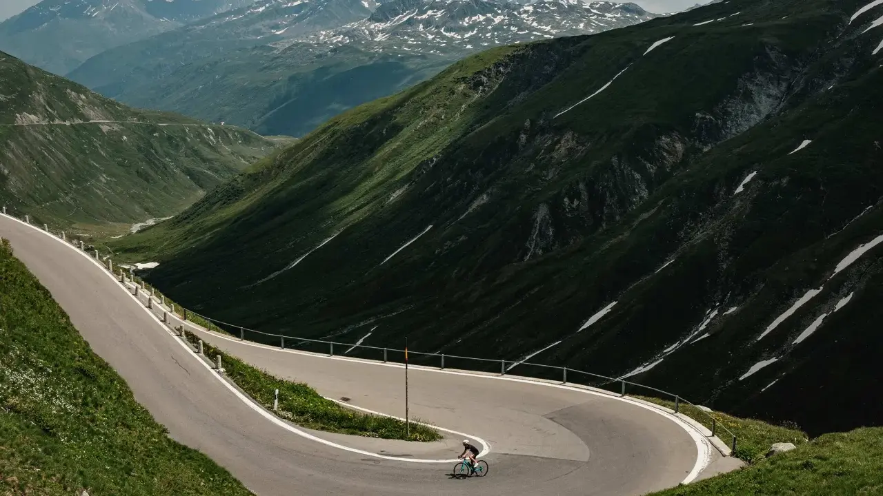 Radfahrer auf einem Transalp Rennrad meistert Serpentinen in den Alpen. Majestätische Bergkulisse mit Schneefeldern.