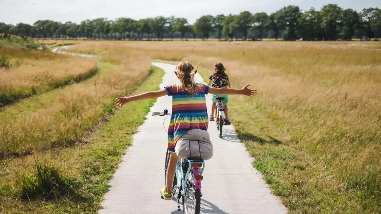 Zwei Mädchen genießen eine Fahrradtour in NRW auf einem Feldweg, umgeben von goldenem Gras und Bäumen.