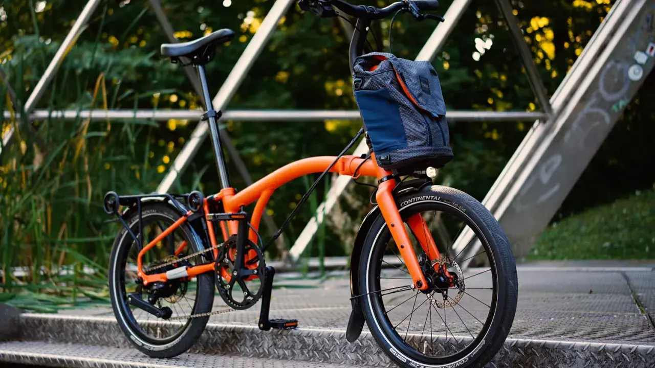 Orange Brompton Electric im Test auf einer Metallbrücke, bereit für die nächste Fahrt.