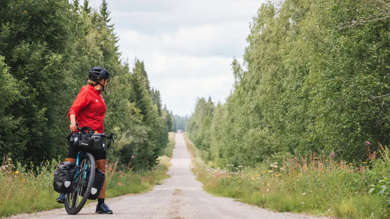 Frauen auf Bikepacking-Tour in Schweden, bereit für die nächste Etappe auf einer einsamen Schotterstraße, umgeben von üppigem Grün.