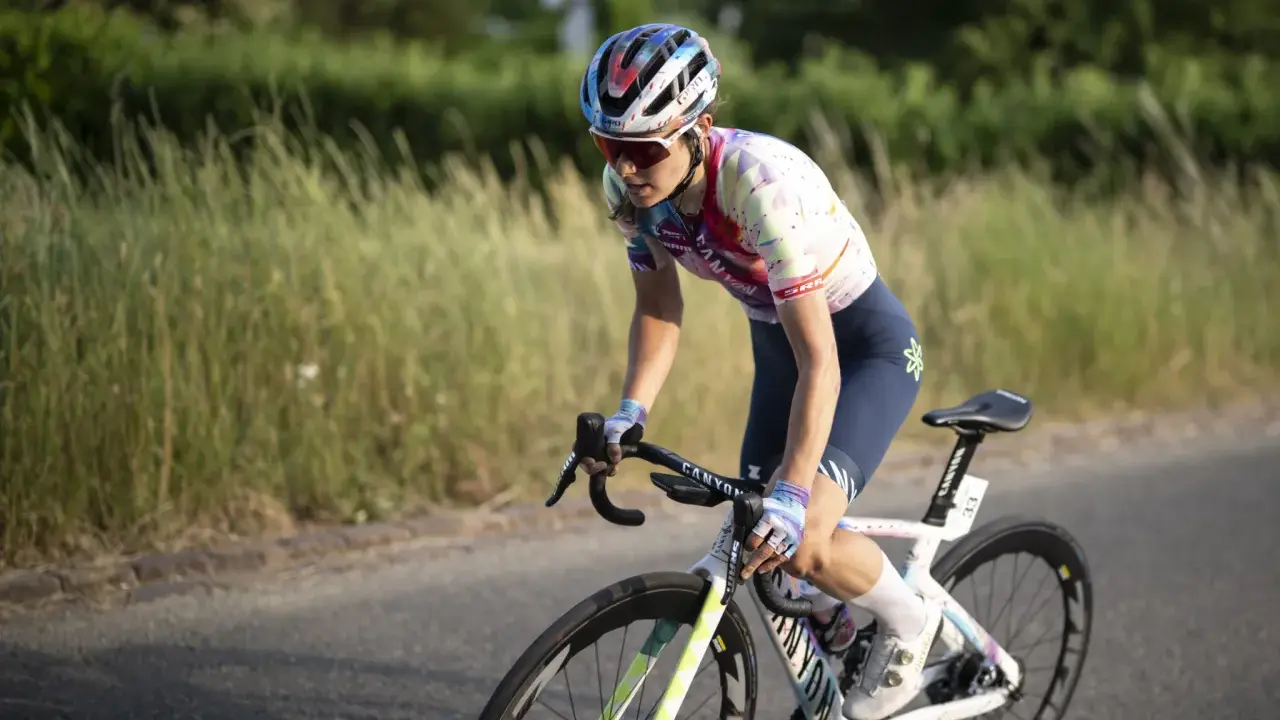 Elise Chabbey in voller Fahrt auf ihrem Rennrad, die Konzentration im Blick, während sie durch eine grüne Landschaft fährt.