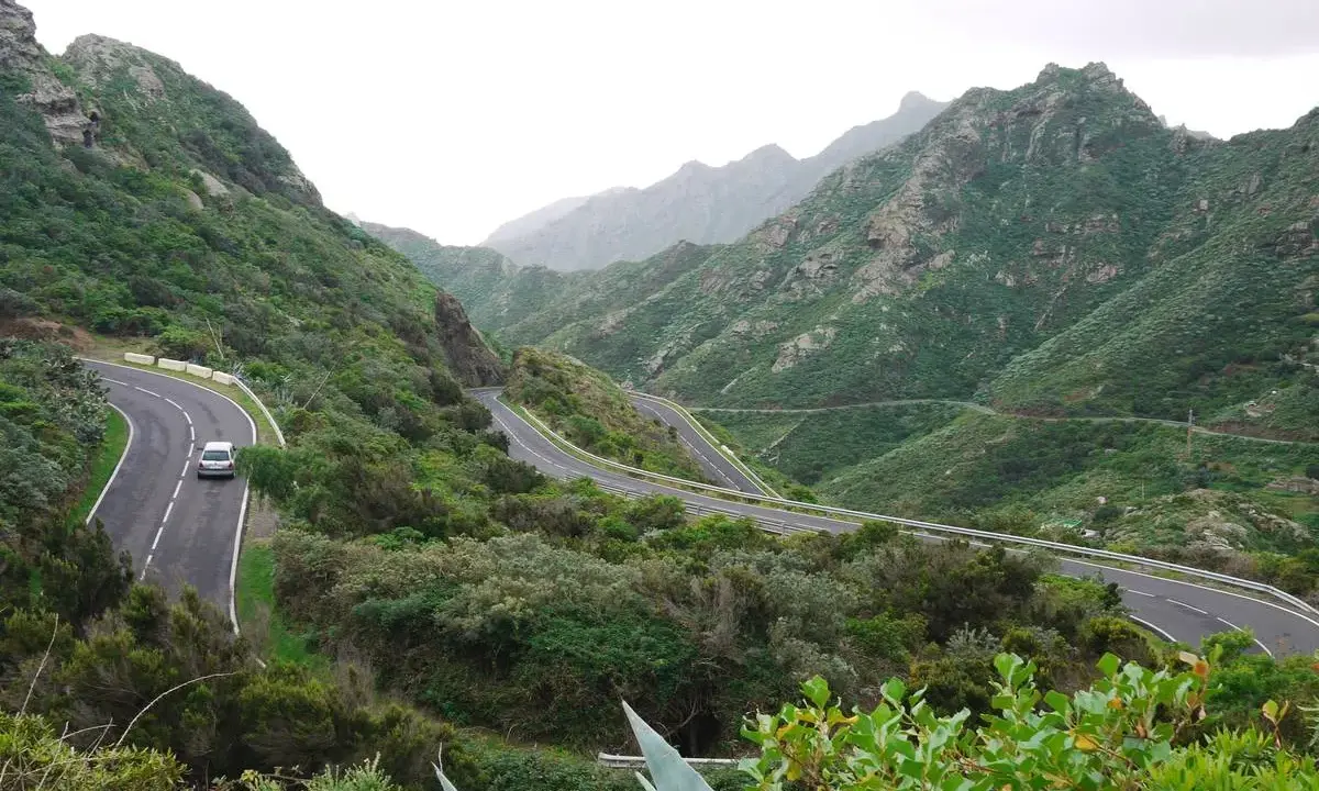 Serpentinenstraße auf Teneriffa, ideal für eine Rennradtour durch grüne Berge. Ein Auto fährt auf der kurvenreichen Straße.
