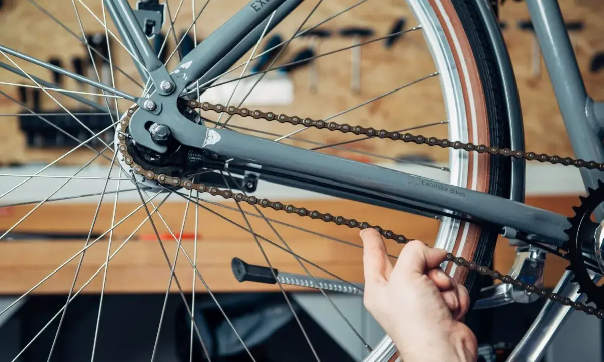 Hand prüft die Spannung der Fahrradkette am Hinterrad eines grauen Fahrrads.