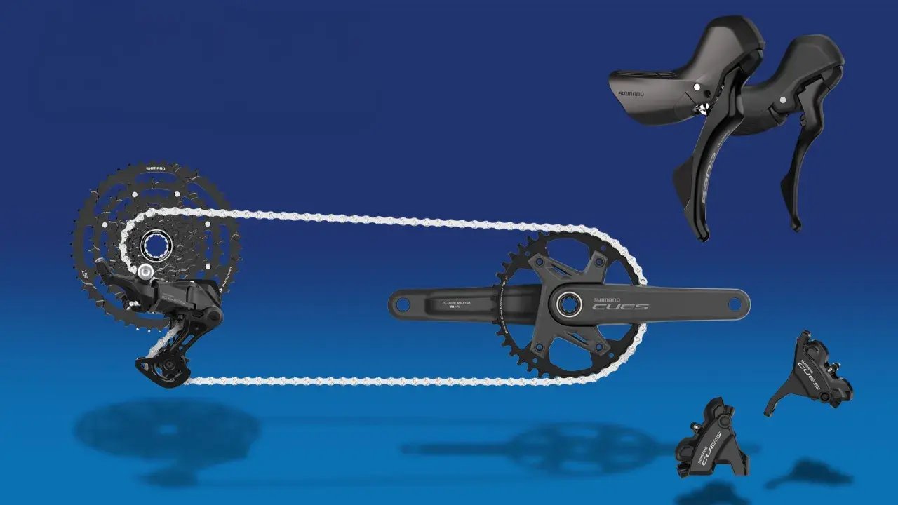 Shimano CUES Fahrradkomponenten: Schaltwerk, Kassette, Kurbelgarnitur und Schalthebel in Schwarz vor blauem Hintergrund.