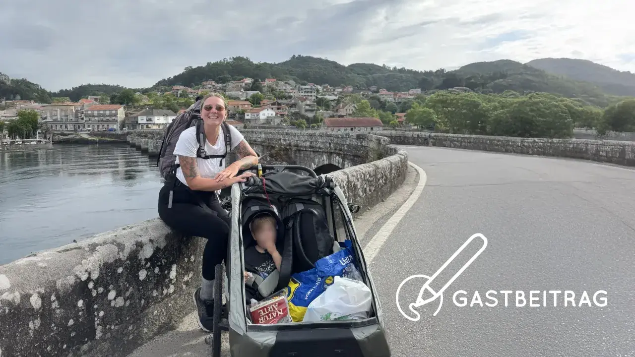 Frau mit Rucksack und Kinderwagen auf einer Brücke, bereit für eine abc tour. Im Hintergrund eine Stadt und Berge.