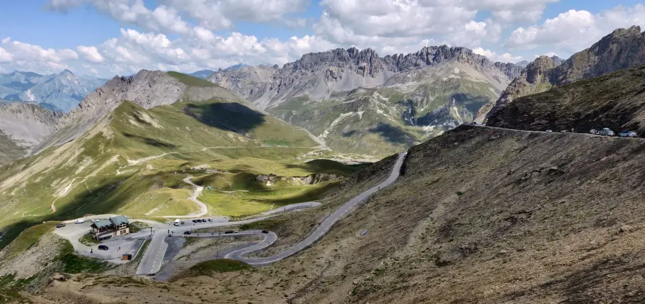 Bergpanorama mit Serpentinenstraße, grasbewachsenen Hängen und schroffen Gipfeln.