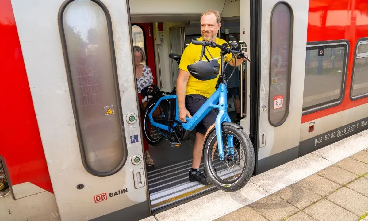 Mann mit blauem E-Bike steigt in den Zug. Perfekt, um das E-Bike im Zug mitzunehmen und die Reise fortzusetzen.