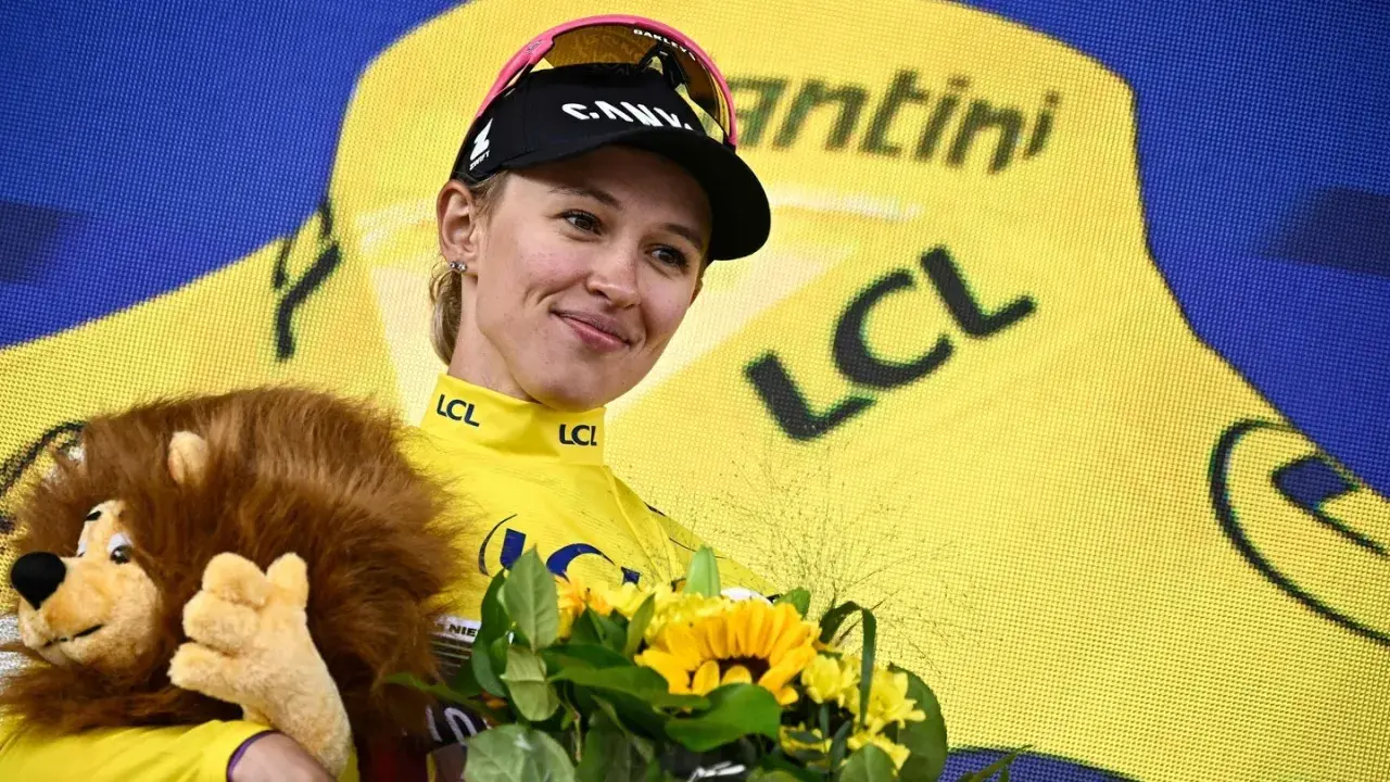 Kasia Niewiadoma strahlt im gelben Trikot, hält einen Löwen-Plüschtier und Blumen.