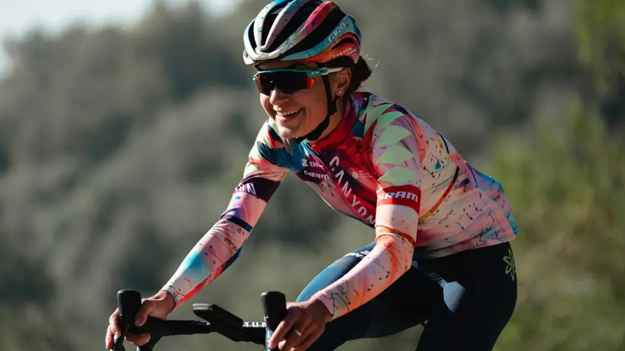 Ricarda Bauernfeind lacht auf ihrem Rennrad, trägt einen bunten Helm und ein auffälliges Trikot mit geometrischen Mustern.