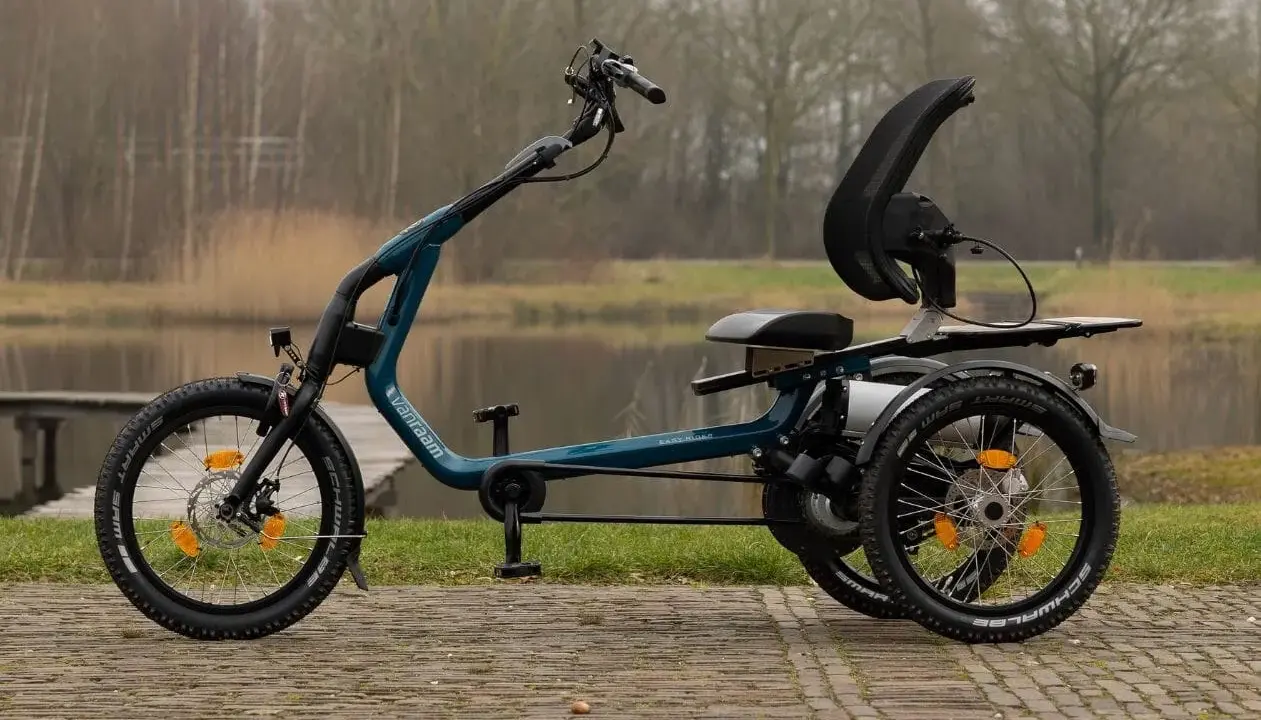 Ein tealfarbenes Easy Rider Bike mit drei Rädern steht am Wasser. Es hat einen bequemen Sitz und eine hohe Rückenlehne.
