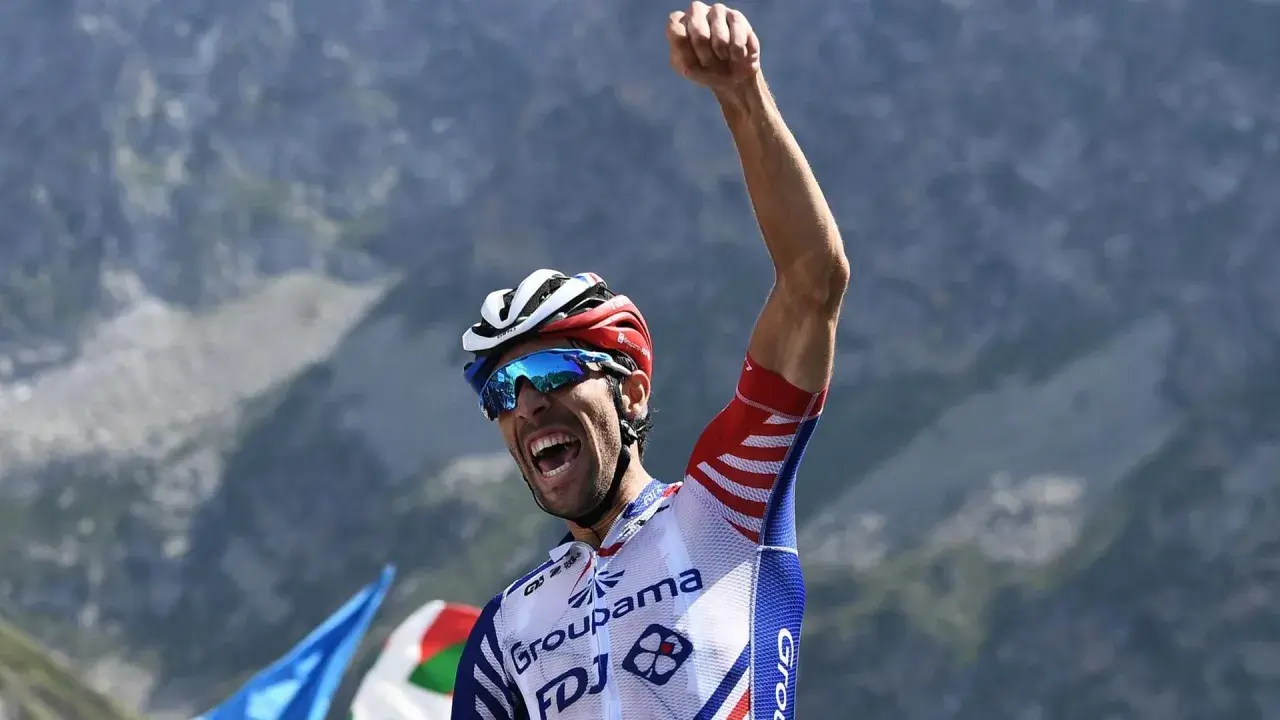 Thibaut Pinot jubelt mit geballter Faust auf einem Berggipfel, die Augen hinter blauen Sonnenbrillen, ein Triumph nach harter Anstrengung.