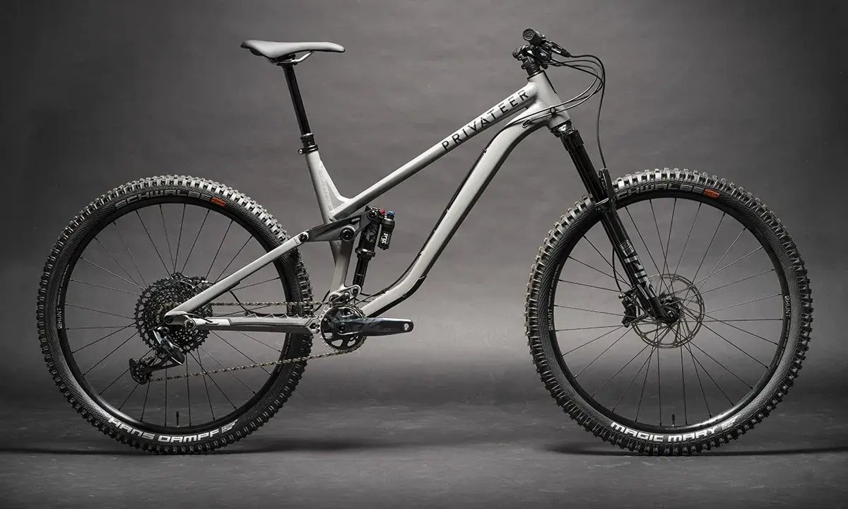 Ein graues Fullsuspension-Mountainbike der Marke Privateer steht auf dunklem Grund. Dieses Bike ist bereit für jedes Abenteuer.