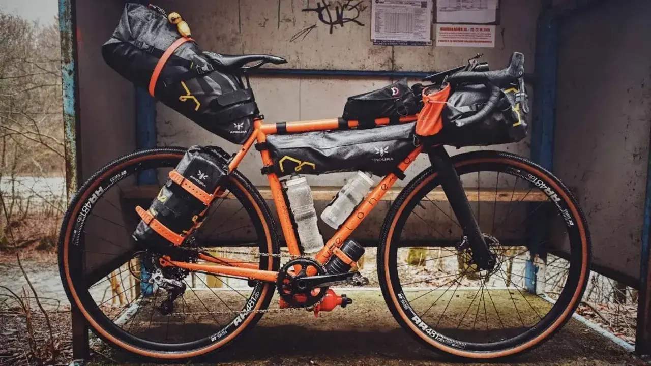 Orange Rennrad mit Bikepacking-Taschen, bereit für Abenteuer.