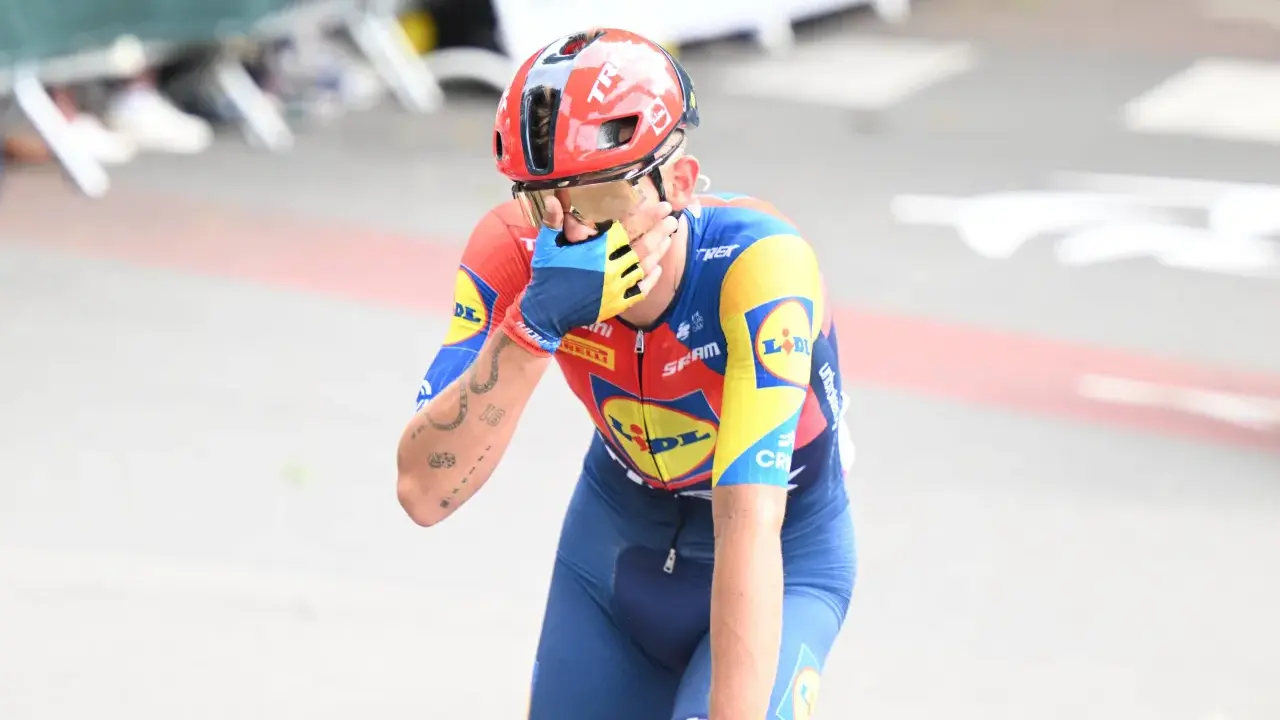 Radfahrer Thibau Nys wischt sich mit der Hand über das Gesicht, trägt einen roten Helm und ein blau-gelbes Trikot.