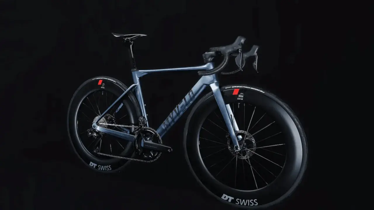 Ein elegantes, hellblaues Rennrad, das myvelo Verona, steht vor schwarzem Hintergrund. Seine aerodynamischen Felgen und die schlanke Silhouette versprechen Geschwindigkeit.