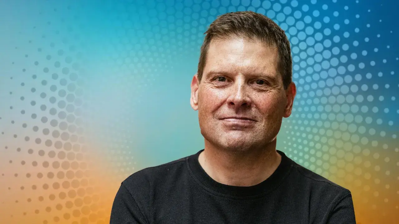 Porträt eines Mannes mit freundlichem Lächeln vor einem bunten Hintergrund. Man fragt sich, was macht Jan Ullrich heute?