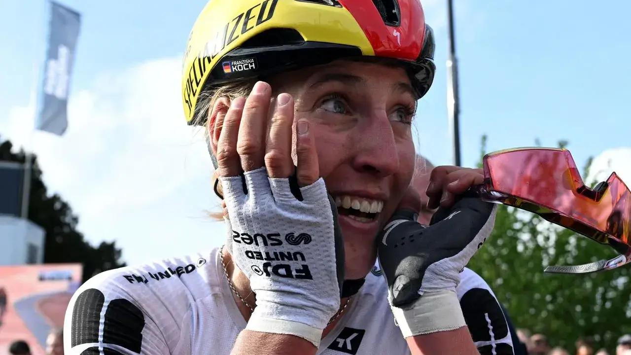 Glückliche Radfahrerin Franziska Koch mit Helm in Deutschlandfarben, die sich die Hände vors Gesicht hält.