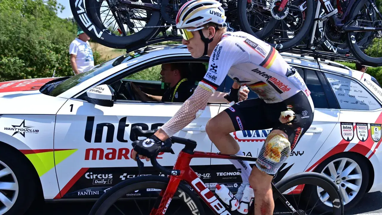 Radfahrer Georg Zimmermann mit aufgeschürftem Knie fährt neben dem Begleitfahrzeug des Teams Intermarché-Wanty.