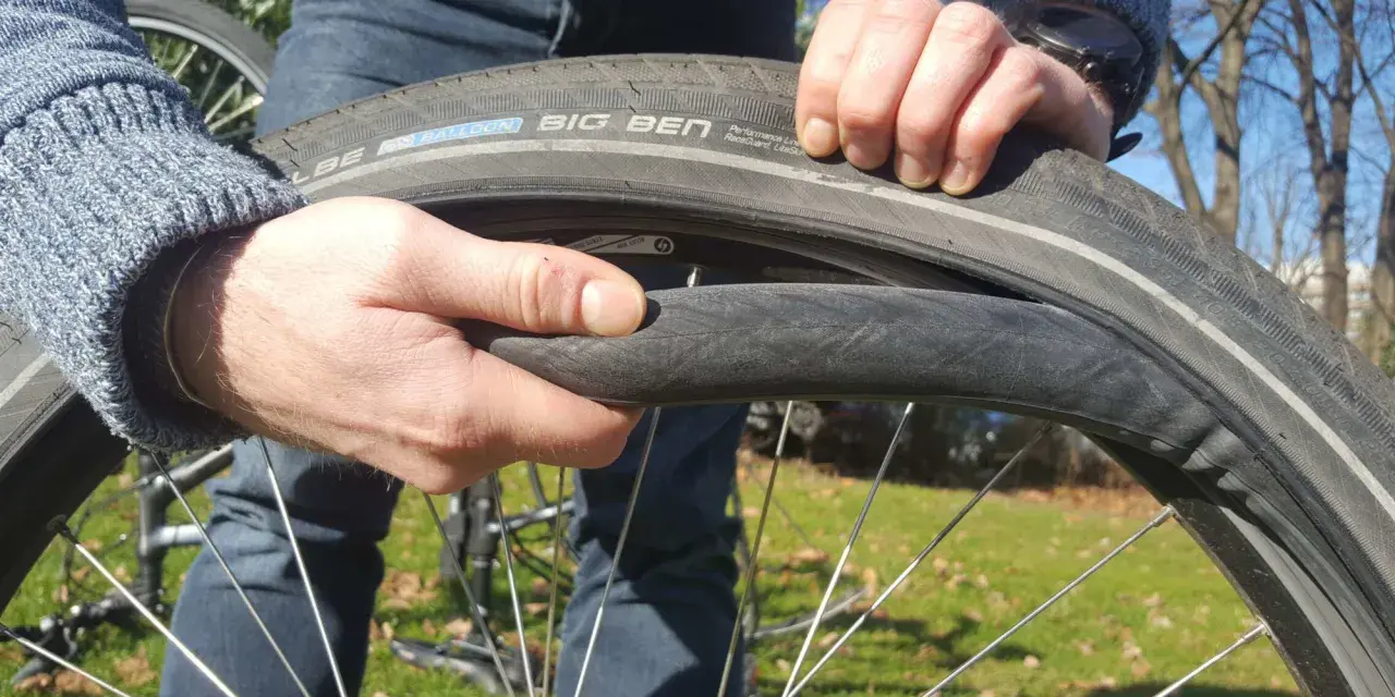 Hände wechseln einen platten Fahrradreifen. Der Reifen ist ein Schwalbe Big Ben.