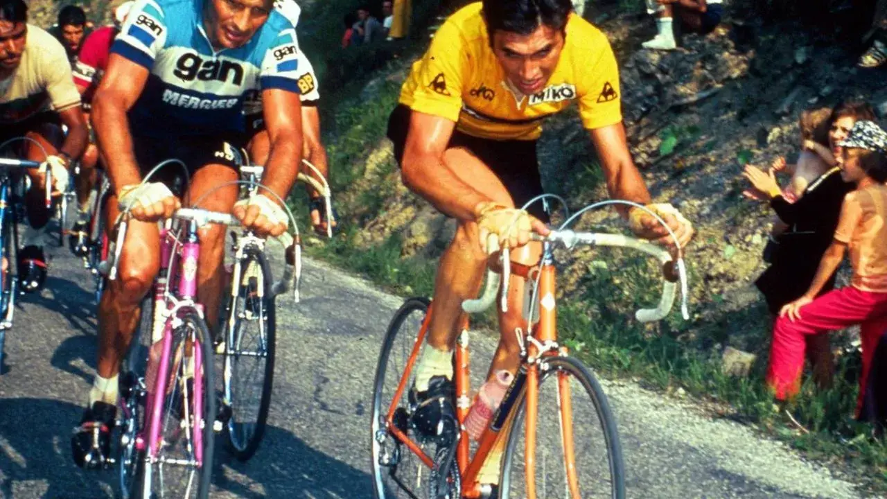 Eddy Merckx heute im Gelben Trikot, kämpft sich einen Berg hinauf. Fans jubeln am Straßenrand.