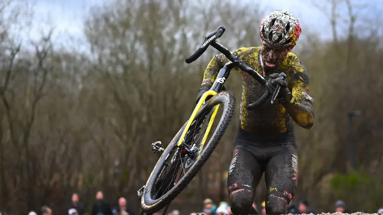 Wout van Aert kämpft sich im Schlamm durch ein hartes Cyclocross-Rennen, sein Körper und Rad sind komplett mit Dreck bedeckt.