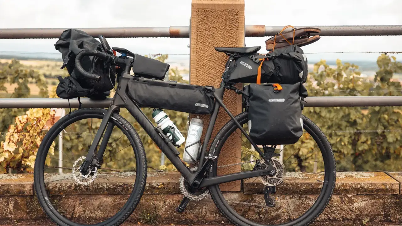 Bereit für die nächste gravel tour: Ein voll beladenes Gravelbike mit Ortlieb-Taschen, Trinkflaschen und sogar Schuhen auf dem Gepäckträger.