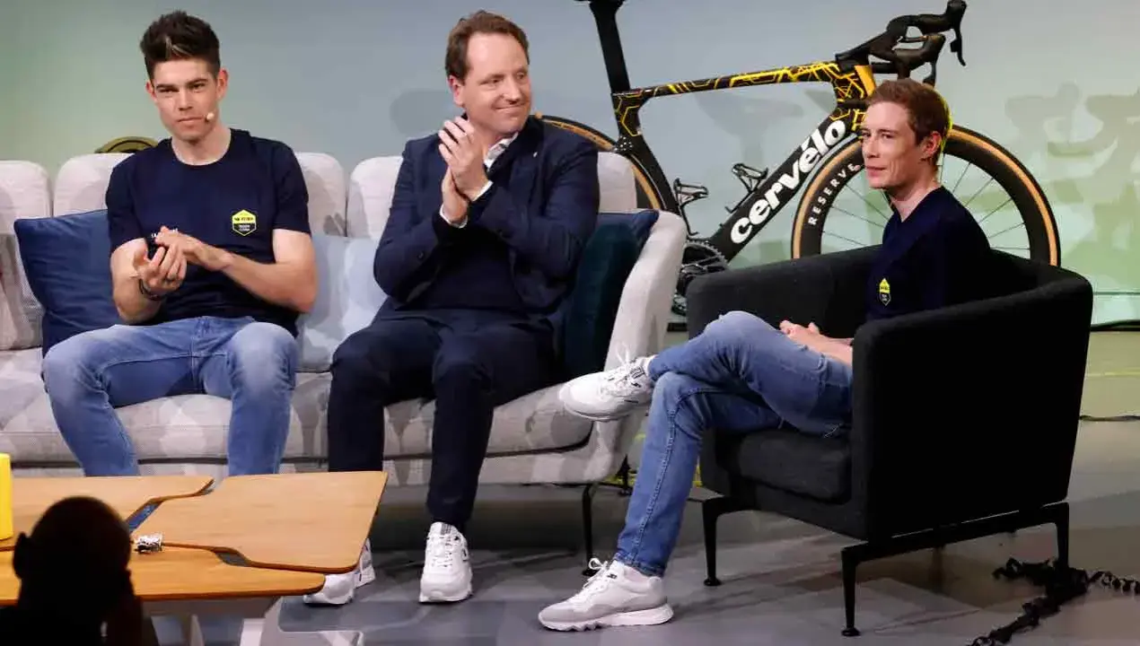 Drei Männer, darunter ein Fahrer von Jumbo-Visma, sitzen auf Sofas vor einem Rennrad.