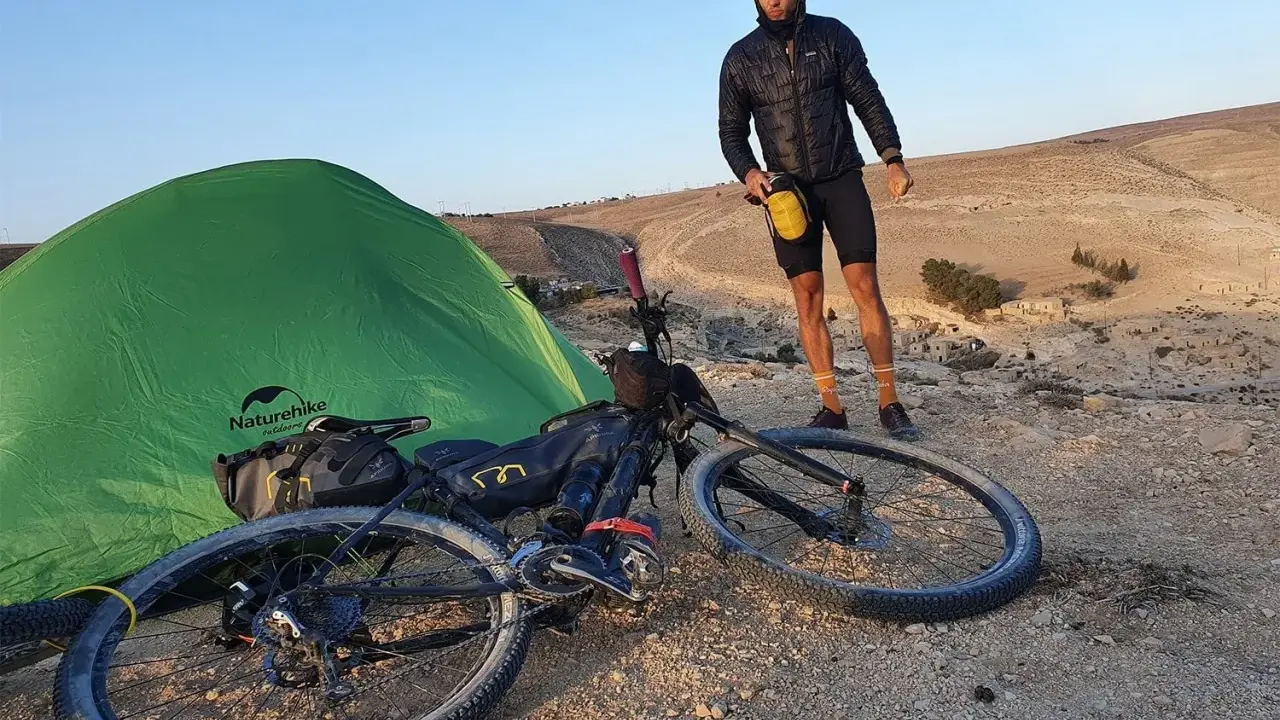 Mann mit Fahrrad und Zelt in bergiger Landschaft, bereit für neue **biking trails**.