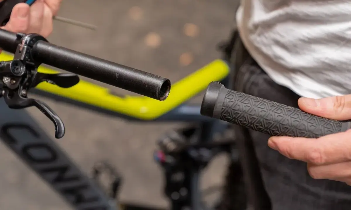 Person wechselt Fahrradgriffe. Der Lenker ist freigelegt, die neue Griff wird bereitgehalten.
