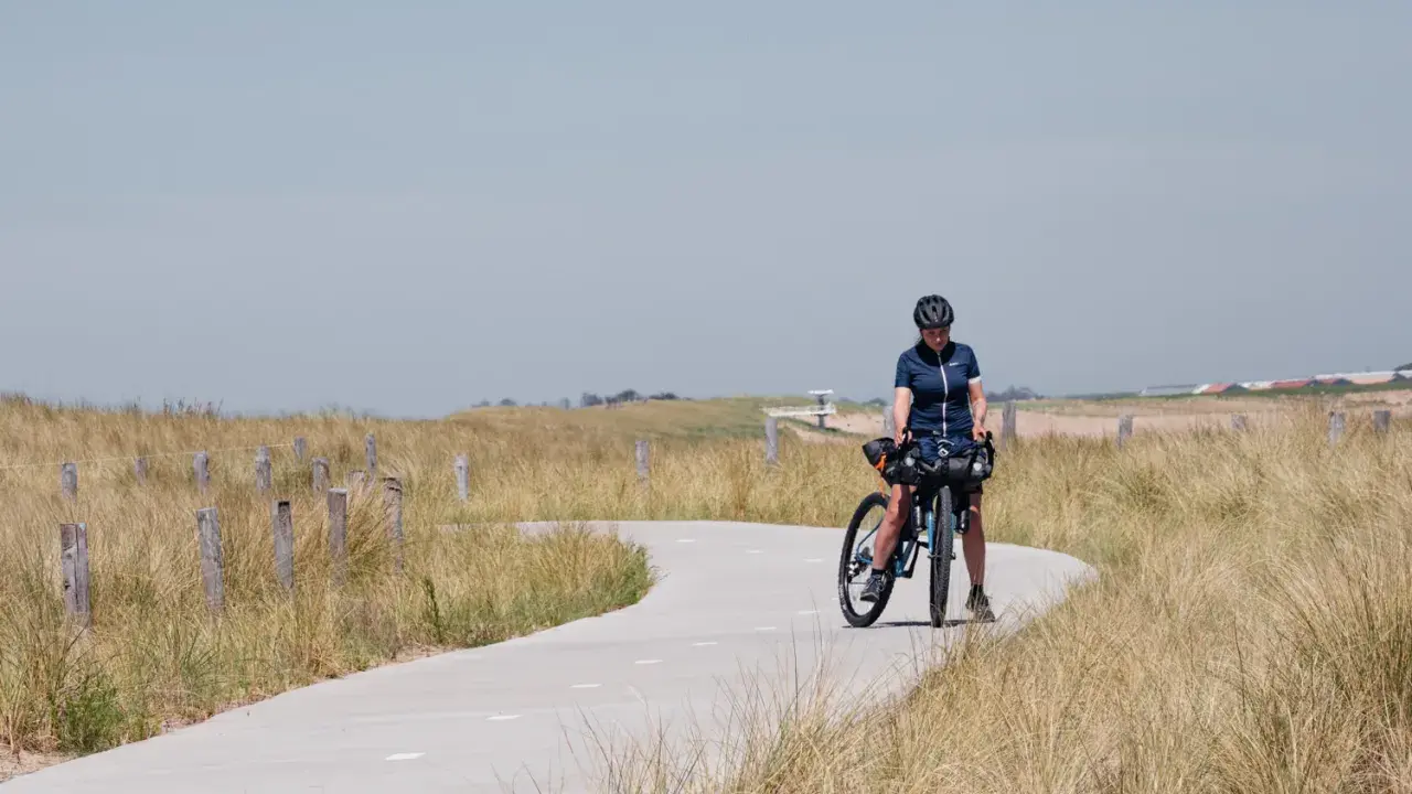 Frau mit Fahrrad auf einer Küstenstraße, bereit für eine Fahrradtour in der Nähe von Amsterdam.