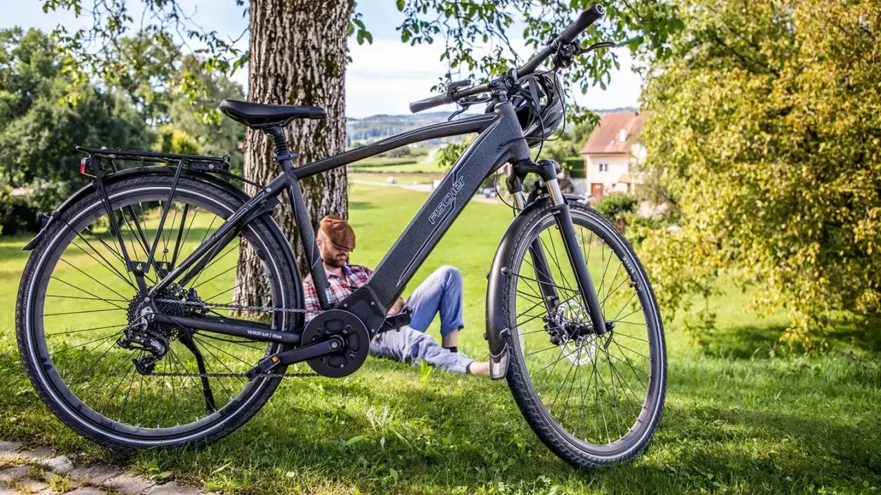 Fischer Viator 6.0i Test: Ein Mann entspannt sich im Schatten eines Baumes neben seinem E-Bike.