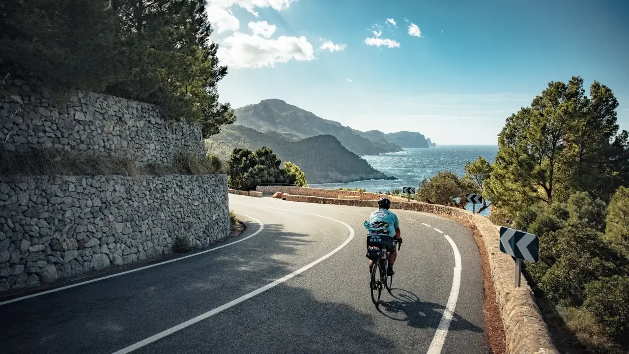 Rennradfahrer auf einer kurvigen Straße mit Blick auf das Meer und die Berge auf Mallorca.