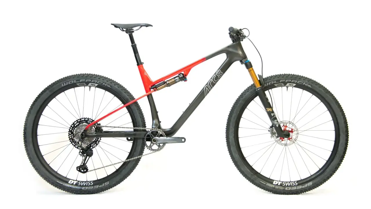 Ein modernes Mountainbike mit Vollfederung, Rahmen in Grau und Rot, Schriftzug "ARC8". Bereit für jedes Abenteuer.