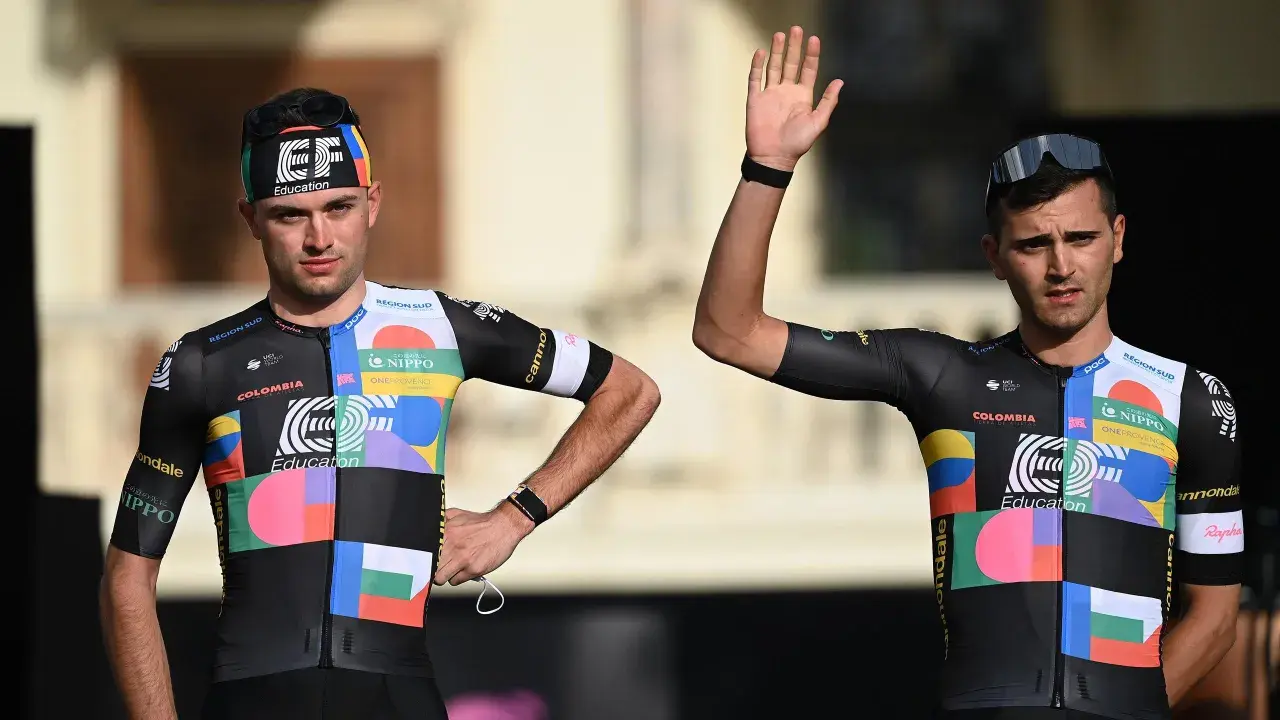 Zwei Radfahrer im bunten Trikot, bereit für den Giro d'Italia. Einer winkt lässig.