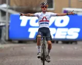 Thomas Pidcock feiert seinen Sieg mit ausgebreiteten Armen. Der Radfahrer trägt ein weißes Trikot mit britischer Flagge und dunkle Hosen.
