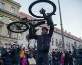 Jonas Deichmann, sichtlich erschöpft, hält sein schlammbedecktes Fahrrad über den Kopf. Eine jubelnde Menge mit Smartphones feiert seine Ankunft.