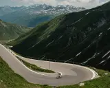 Radfahrer auf einem Transalp Rennrad meistert Serpentinen in den Alpen. Majestätische Bergkulisse mit Schneefeldern.