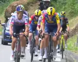 Radsportler im Peloton, darunter Cian Uijtdebroeks, kämpfen sich bergauf. Motorräder und ein Auto begleiten das Rennen.