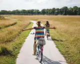 Zwei Mädchen genießen eine Fahrradtour in NRW auf einem Feldweg, umgeben von goldenem Gras und Bäumen.