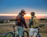Zwei Radfahrer blicken bei Sonnenuntergang auf die Landschaft. Ein Mann zeigt in die Ferne, vielleicht auf den Stoneman Arduenna.
