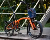 Orange Brompton Electric im Test auf einer Metallbrücke, bereit für die nächste Fahrt.