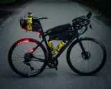 Bereit für ultra cycling: Rennrad mit Bikepacking-Taschen, Trinkflaschen und Lichtern auf asphaltierter Straße.