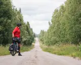 Frauen auf Bikepacking-Tour in Schweden, bereit für die nächste Etappe auf einer einsamen Schotterstraße, umgeben von üppigem Grün.