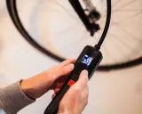 Hände halten eine digitale Luftpumpe, die den Druck in Bar anzeigt, bereit, den Fahrradreifen aufzufüllen.