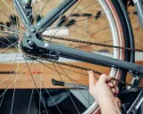 Hand prüft die Spannung der Fahrradkette am Hinterrad eines grauen Fahrrads.