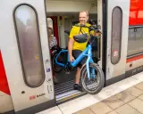 Mann mit blauem E-Bike steigt in den Zug. Perfekt, um das E-Bike im Zug mitzunehmen und die Reise fortzusetzen.