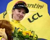 Kasia Niewiadoma strahlt im gelben Trikot, hält einen Löwen-Plüschtier und Blumen.