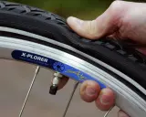 Daumen prüft den luftdruck reifen eines Fahrrads. Der Reifen ist leicht eingedrückt, was auf zu wenig Luft hindeutet.