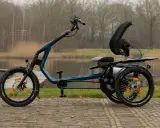 Ein tealfarbenes Easy Rider Bike mit drei Rädern steht am Wasser. Es hat einen bequemen Sitz und eine hohe Rückenlehne.